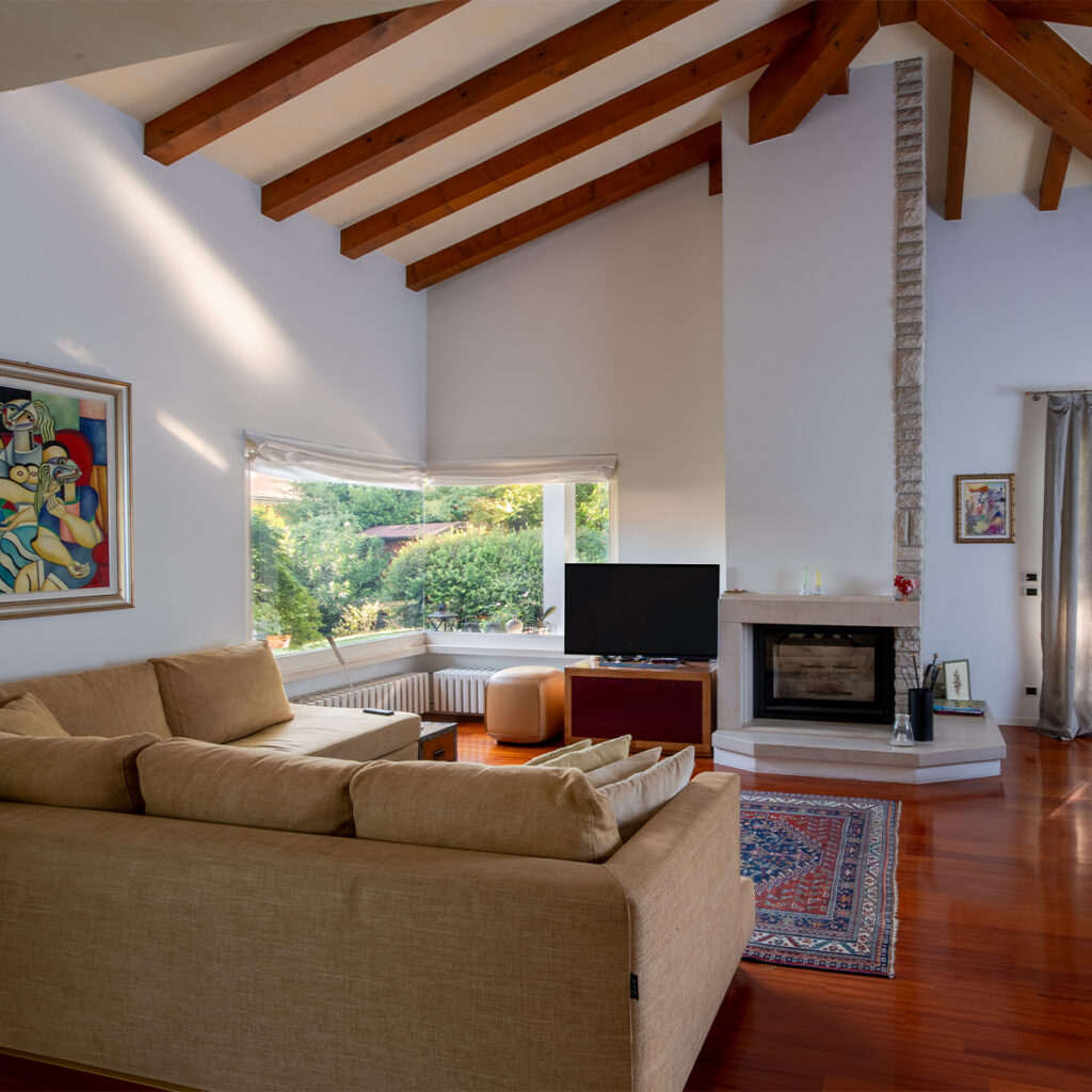 il salotto della casa nel verde con vetrata ad angolo, camino e soffitto con le travi a vista.