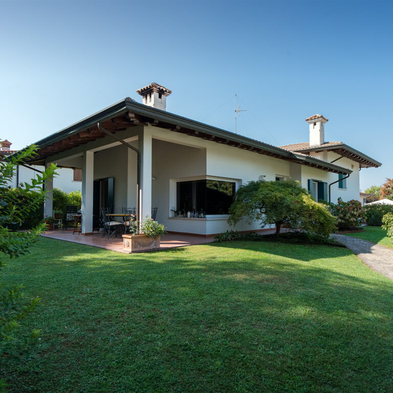 La facciata esterna della casa vista da un angola del giardino ci fa vedere la vetrata ad angolo e la dona da pranzo esterna.