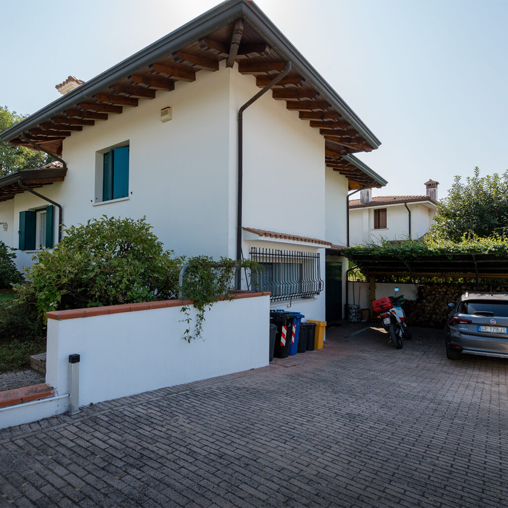 La casa nel verde vista dal lato della pergola di gelsomino che copre le auto.