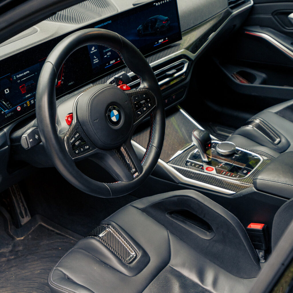 Il Posto di Guida della BMW M3 Compietition con sedili e volante sportivi, dettagli in carbonio e display touchscreen da 12,3 pollici.